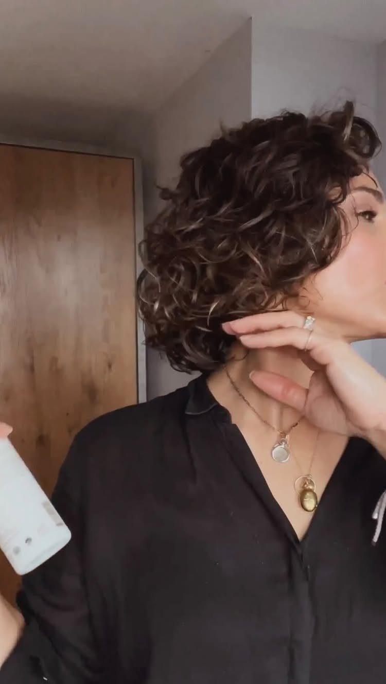 Woman with short curly brown hair wearing a black shirt and gold necklaces.