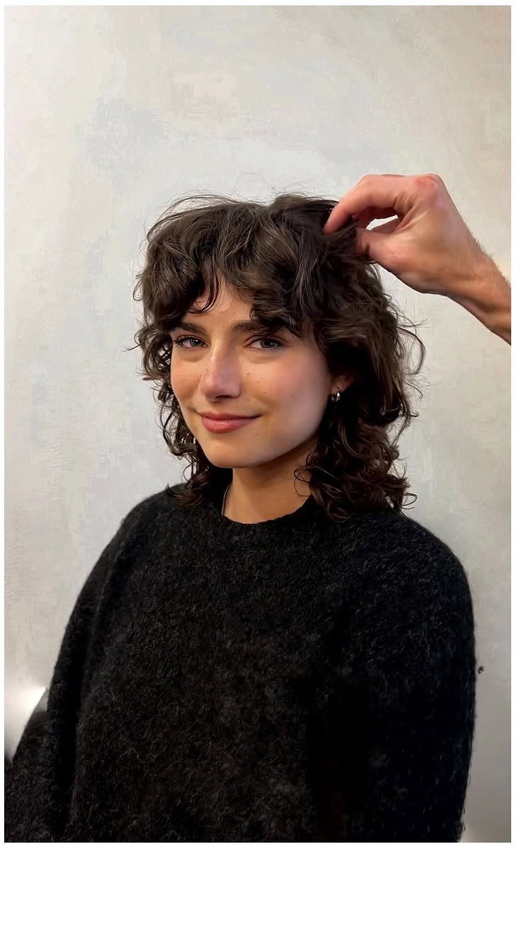 Woman with a short brown shag haircut and curly fringe wearing a black sweater.
