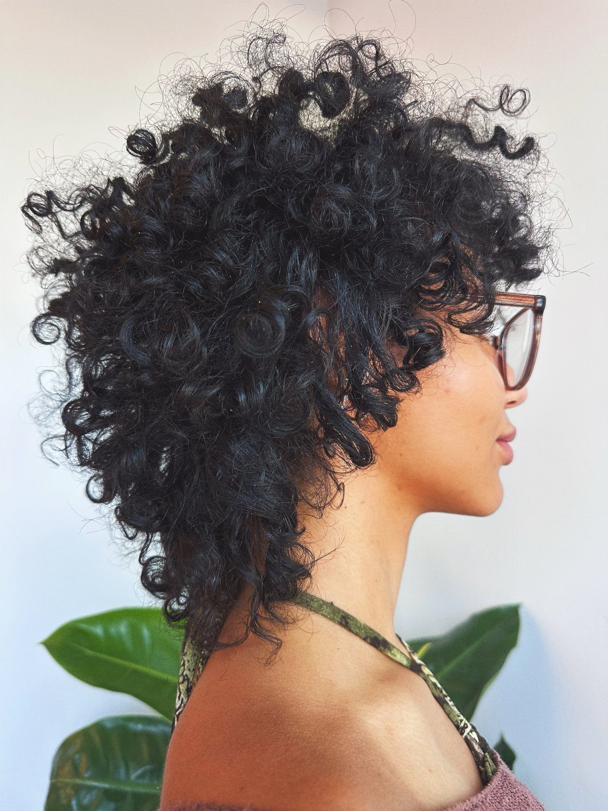 Person with voluminous curly black pixie cut and glasses in side profile view.