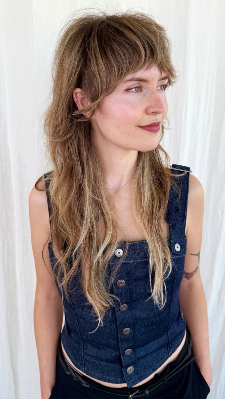 Woman with a layered wolf cut hairstyle and bangs wearing a denim vest.