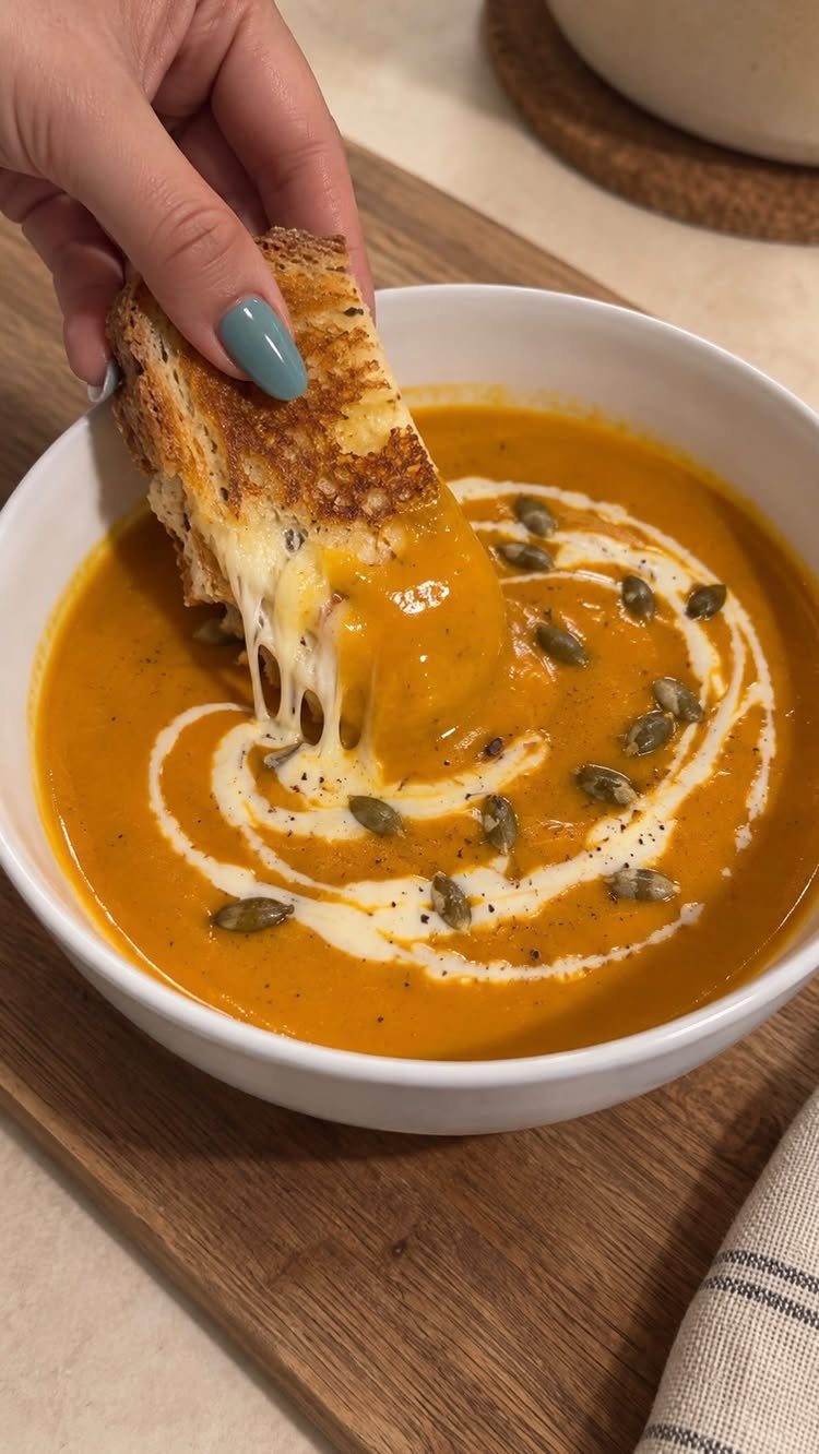 Pumpkin soup with cream and seeds being eaten with a cheesy toast dip.