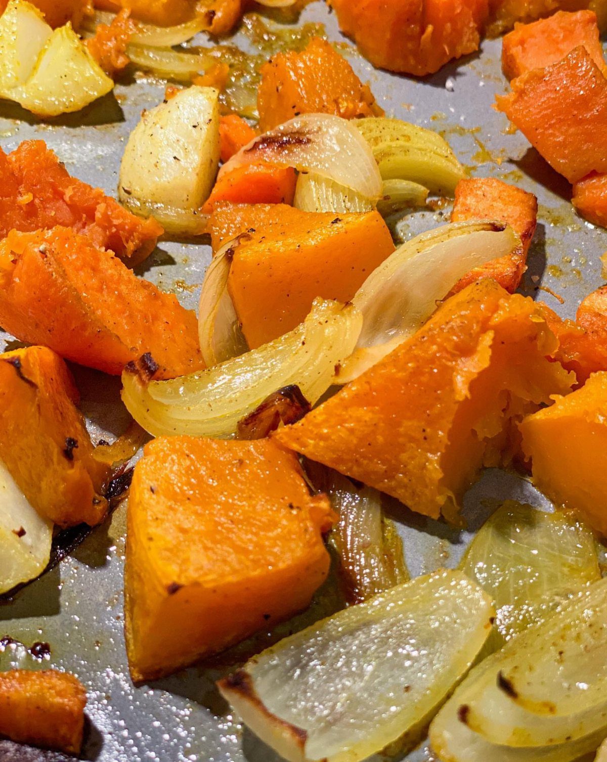 Roasted sweet potato chunks and white onion wedges on a metal baking tray.