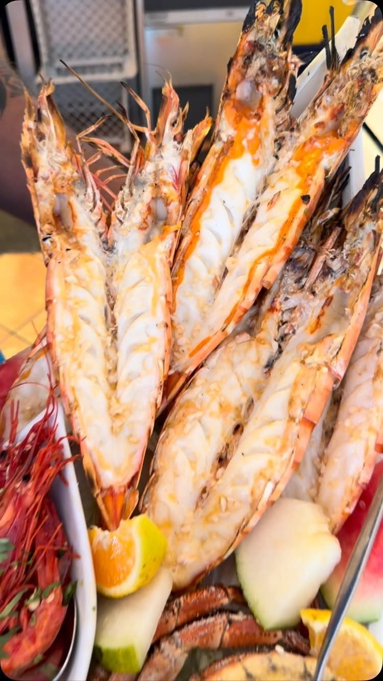 Grilled butterflied prawns on a platter with lemon wedges and fresh fruit.